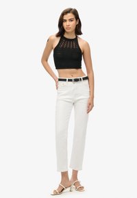 Top corto de ganchillo negro con un diseño texturizado, combinado con jeans rectos blancos y sandalias de tacón blancas. Cinturón negro con hebilla plateada.