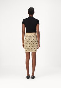 Un haut noir à manches courtes associé à une jupe crayon beige texturée avec un motif géométrique noir, porté avec des chaussures noires.
