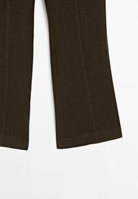 Pantalon marron à jambes larges avec coutures visibles sur fond blanc, montrant la moitié inférieure des jambes du vêtement.