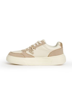Sneaker beige e crema basse con chiusura frontale a lacci, suola spessa e ciondolo con logo "M" metallizzato sul lato.