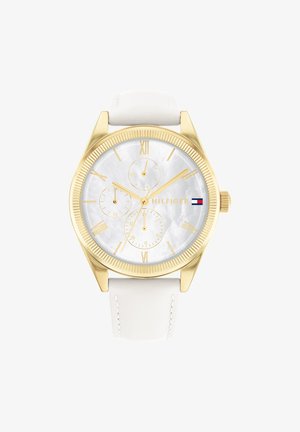 Złocisty zegarek na nadgarstek z białym skórzanym paskiem, białą tarczą, trzema subtarczami, rzymskimi cyframi oraz logo Tommy Hilfiger z flagą na tarczy.