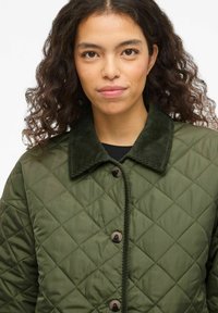 Veste matelassée vert olive avec un col en velours côtelé, ornée de boutons arrondis et d'une surface texturée, idéale pour les temps plus frais.