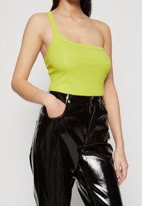 Top senza maniche di un verde lime asimmetrico con texture a coste, abbinato a pantaloni neri in similpelle lucida a vita alta con tasche laterali.