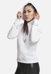 Valge kapuutsiga sweatshirt, millel on paelad ja ribit artlikud, kantud mustade retuusidega. Pehme materjal, keha lähedane lõige ja minimalistik stiil.