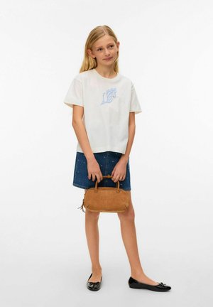 Ung pige med langt blondt hår iført hvidt t-shirt med print og denimnederdel, der holder en lille brun håndtaske og står mod en hvid baggrund.