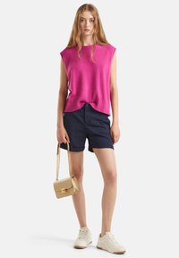 Jasně růžový bezrukávový svetr, námořnické šortky, bílé tenisky a malá zlatá kabelka s řetízkovým páskem, se sponou.