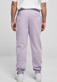 Lilafarbene Jogginghose mit elastischen Bündchen, Kordelzugbund und einer Tasche auf der Rückseite. Getragen mit weißen Turnschuhen. Weiches, strukturiertes Material.