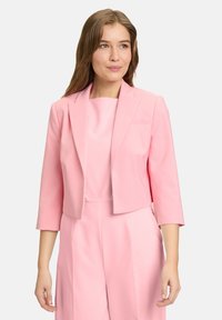 Skrócony różowy żakiet z rękawami o długości trzech czwartych, gładki materiał, wykładany kołnierz i jedna kieszeń na klatce piersiowej, noszony na dopasowanej bluzce.