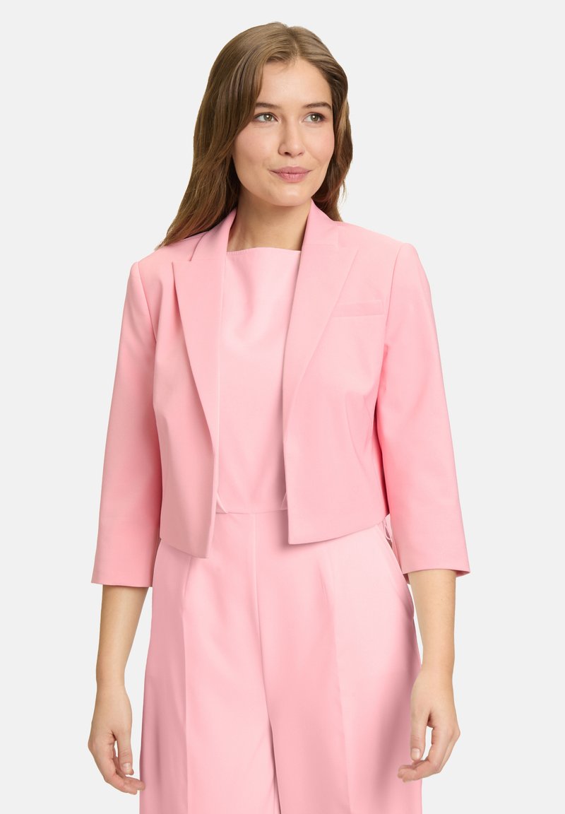 Skrócony różowy żakiet z rękawami o długości trzech czwartych, gładki materiał, wykładany kołnierz i jedna kieszeń na klatce piersiowej, noszony na dopasowanej bluzce.