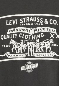 T-shirt noire avec une impression graphique blanche comportant du texte et des illustrations de deux chevaux et de figures, détaillée par une texture craquelée.
