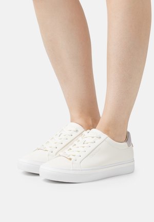 Białe skórzane sneakersy o gładkiej fakturze, z sznurowanym zapięciem, miękkim szarym akcentem na tyle oraz grubą białą gumową podeszwą.