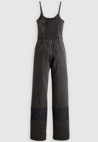 Combinaison en denim noir avec bretelles spaghetti, dos smocké, jambes larges, poignets foncés contrastants et deux poches arrière.