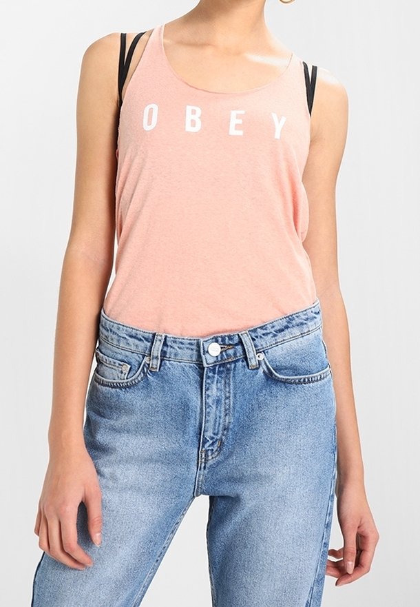 Ljusrosa linne med vitt "OBEY"-tryck, kombinerat med höga blå jeans i denim. Har tunna axelband och en avslappnad passform.