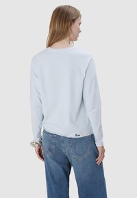 Hellblaues Langarm-T-Shirt mit rundem Halsausschnitt, mit eingesticktem "True Religion"-Logo am Saum. Kombiniert mit hellblauen Jeans.