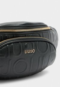 Borsa in pelle nera con motivo a logo impresso, dettagli in cerniera dorata e forma arrotondata. Presenta una finitura liscia e testurizzata.