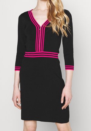 Czarna sukienka o długości do kolan z rękawami do połowy przedramienia, ozdobiona jaskraworóżowymi paskami na dekolcie, talii i mankietach rękawów, noszona przez kobietę.