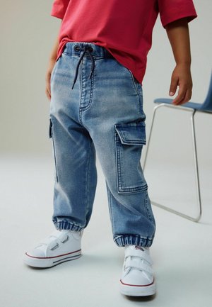 Lyseblå cargos i denim med elastiske manchetter og snøre i taljen; har to sidelommer og afslappet pasform. Kombineret med hvide sneakers.