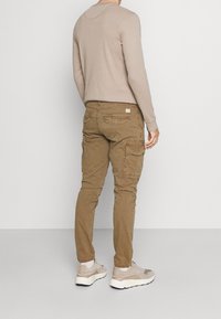 Khaki spodnie cargo z kieszeniami bocznymi, w połączeniu z jasnobeżową koszulą z długim rękawem oraz szaro-białymi trampkami. Casualowy design, elastyczne mankiety.