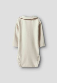 Kremowy bodysuit z długim rękawem i okrągłym dekoltem, z brązową linią akcentującą przy kołnierzyku oraz zapięciami na napy na dole. Wykonany z miękkiego bawełnianego materiału.
