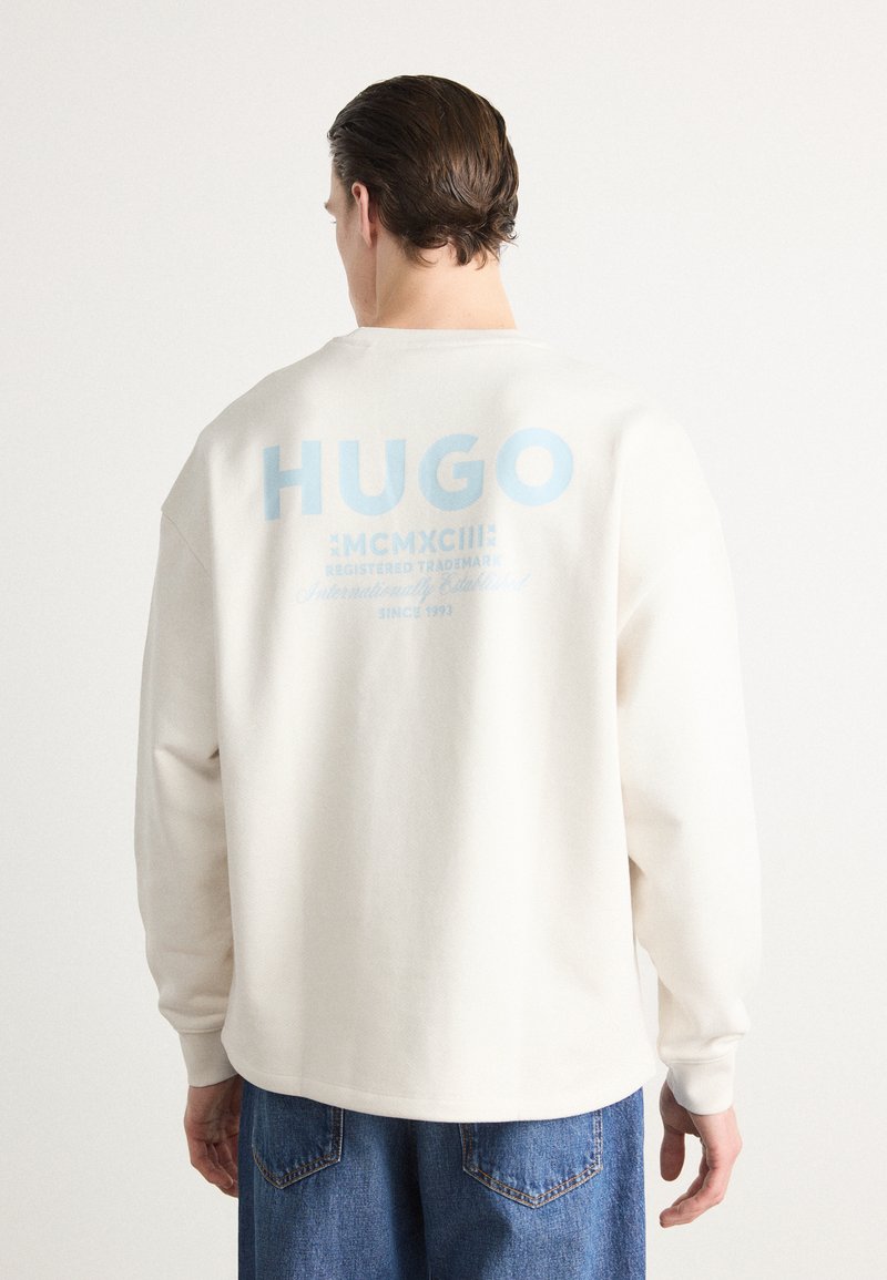 Fehér pamut pulóver kék "HUGO" felirattal és részletekkel a hátsó oldalon. Hosszú ujjú és laza szabású. Minimalista dizájn, minta nélkül.