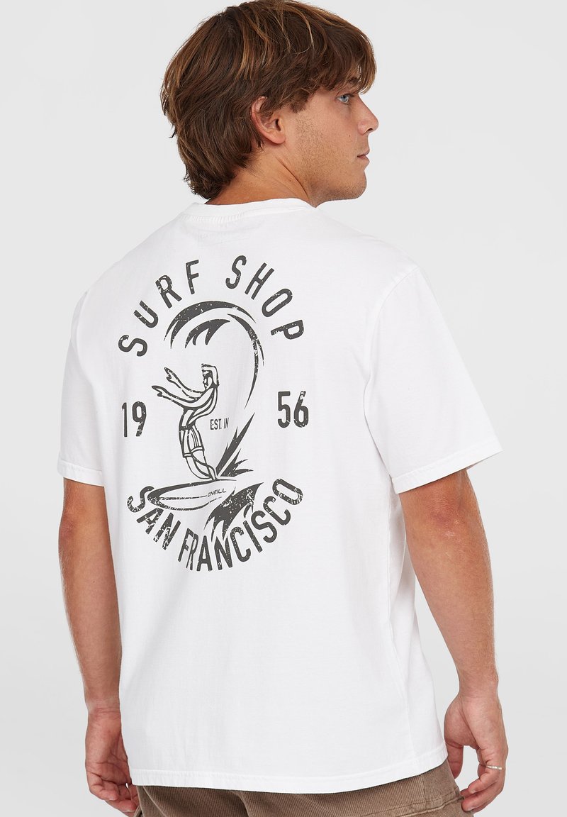 Bílý bavlněný tričko s černým grafickým potiskem na zadní straně, zobrazující surfaře a text "SURF SHOP SAN FRANCISCO 1956."