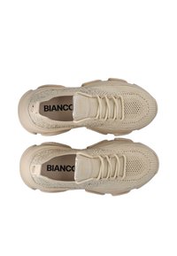 Beige Strick-Sneaker mit strukturiertem Obermaterial, glänzenden Akzenten und einer gepolsterten Sohle, ausgestattet mit einem Schnürdesign und prominenter Markenkennzeichnung.