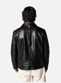 Veste en cuir noir avec une texture lisse, un design ajusté et un distintif onglet rouge à l'arrière. Présente des poignets zippés et des poches latérales.