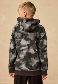 Kapucnis pulóver szürke és fekete katonai mintával, a hátoldalán finom, textúrázott kialakítással szereplő "NEW YORK" felirattal.