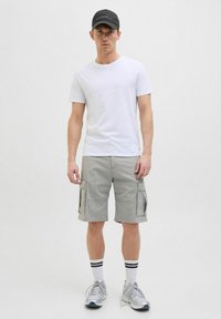 Weißes T-Shirt mit Rundhalsausschnitt kombiniert mit grauen Cargo-Shorts mit Seitentaschen, ergänzt durch eine schwarze Kappe und weiße Socken mit schwarzen Streifen.