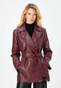 Burgunderfarbene Kunstleder-Trenchcoat mit tailliertem Schnitt, schmalem Kragen und seitlichen Taschen, ausgestattet mit einer glatten, glänzenden Textur.