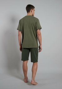 Camiseta de manga corta a rayas en verde oliva combinada con pantalones cortos sólidos en verde oliva hasta la rodilla. Confeccionada en una tela suave y ligera.