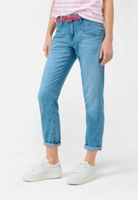 Pantalones vaqueros de denim azul claro con los puños enrollados, combinados con un cinturón rosa y zapatillas blancas. Una camiseta a rayas rosa y blanca añade contraste de color.