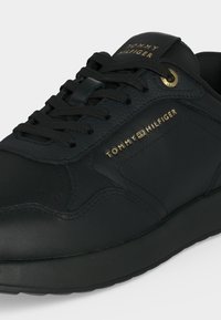 Baskets en cuir noir avec lacets noirs, logo Tommy Hilfiger doré sur le côté et la languette, coutures détaillées et semelle en caoutchouc.