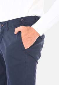 Chino in cotone navy con una texture liscia, dotato di una tasca frontale e chiusura con bottone. Design elegante con dettagli di cucitura discreti.