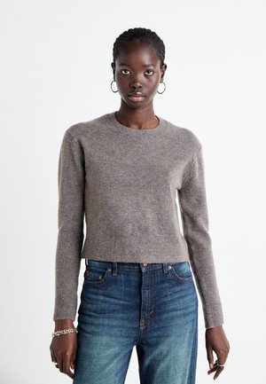 Pull marron coupé avec des manches longues, un col rond et une texture douce, associé à un jean bleu taille haute avec un léger dégradé.