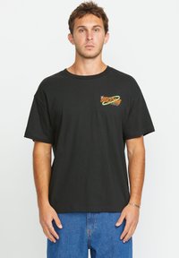 Schwarzes Baumwoll-T-Shirt mit Rundhalsausschnitt und kurzen Ärmeln, versehen mit einem bunten "VOLCOM"-Grafikdesign auf der linken Brust.