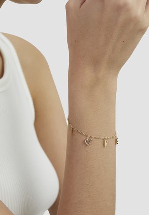 Gold-tone bracelet with chain links featuring letter charms "L," heart-shaped charm with rhinestones, and letter "V," against skin tone.