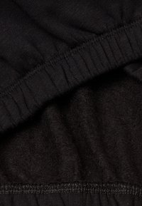 Černý oděv s jemnou, texturovanou tkaninou a nařaseným, elastickým pasem. Viditelné švy podél okraje.