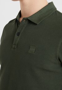 Polo shirt vert foncé avec col et un seul bouton noir, arborant un petit logo BOSS brodé sur la poitrine.