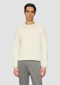 Jasno kremowa koszula polo z długim rękawem o miękkiej teksturze, z klasycznym kołnierzykiem i prążkowanymi mankietami. W połączeniu z szarymi spodniami.
