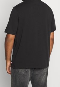 Camiseta negra de manga corta hecha de algodón con un ajuste relajado. Presenta una pequeña etiqueta con el logo en el dobladillo y una textura lisa y sencilla.