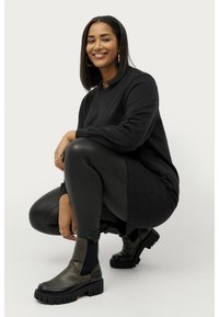 Haut à manches longues noir associé à des leggings noirs. Les chaussures présentent du cuir noir et vert foncé avec une semelle épaisse et des panneaux élastiques sur les côtés.