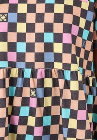 Tissu à carreaux coloré avec des carrés noirs, roses, bleus, jaunes et verts. Ourlet froncé et un petit détail brodé dans le motif.
