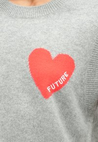 Pull gris avec un grand motif de cœur rouge et le mot "FUTURE" en blanc. La texture est douce, avec un col rond classique et des poignets côtelés.