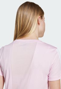 Light pink sports shirt featuring a mesh panel on the back and short sleeves. Smooth texture with ribbed accents along the shoulders.