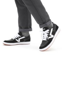 Svarta och grå låga sneakers med vita snören, med en texturerad ovandel och en distinkt vit logotyp på sidan. Gummisula med accenter.