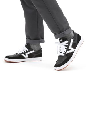 Černé a šedé nízké tenisky s bílými tkaničkami, se strukturovaným svrškem a výrazným bílým logem na boku. Gumená podrážka s akcenty.