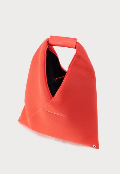 Κόκκινη τρίγωνη υφασμάτινη τσάντα με επενδυμένη λαβή και μικρή μεταλλική λεπτομέρεια κουμπιού στη κάτω γωνία, σε απλό φόντο.