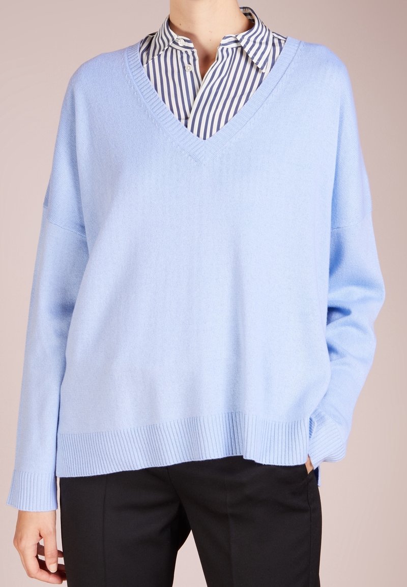 Ljusblå, oversized v-ringad tröja i mjukt stickat material. Har ribbade ärmslut och nederkant, lager på lager över en vit och blårandig skjorta.
