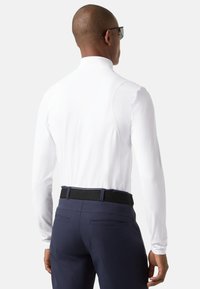 Hvid skjorte med lange ærmer og høj krave, parret med mørkeblå bukser, der har et sort bælte og to baglommer. Glat tekstur og tætsiddende design.